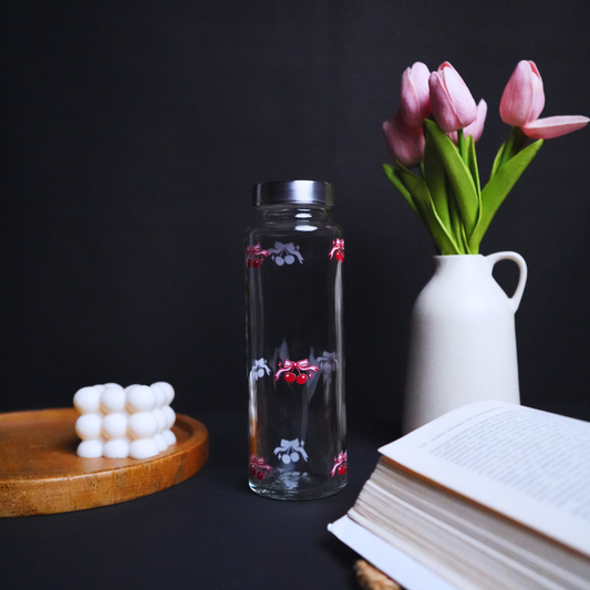 Clear glass bottle with floral design, white vase with pink tulips, wooden coaster, and open book on a dark background