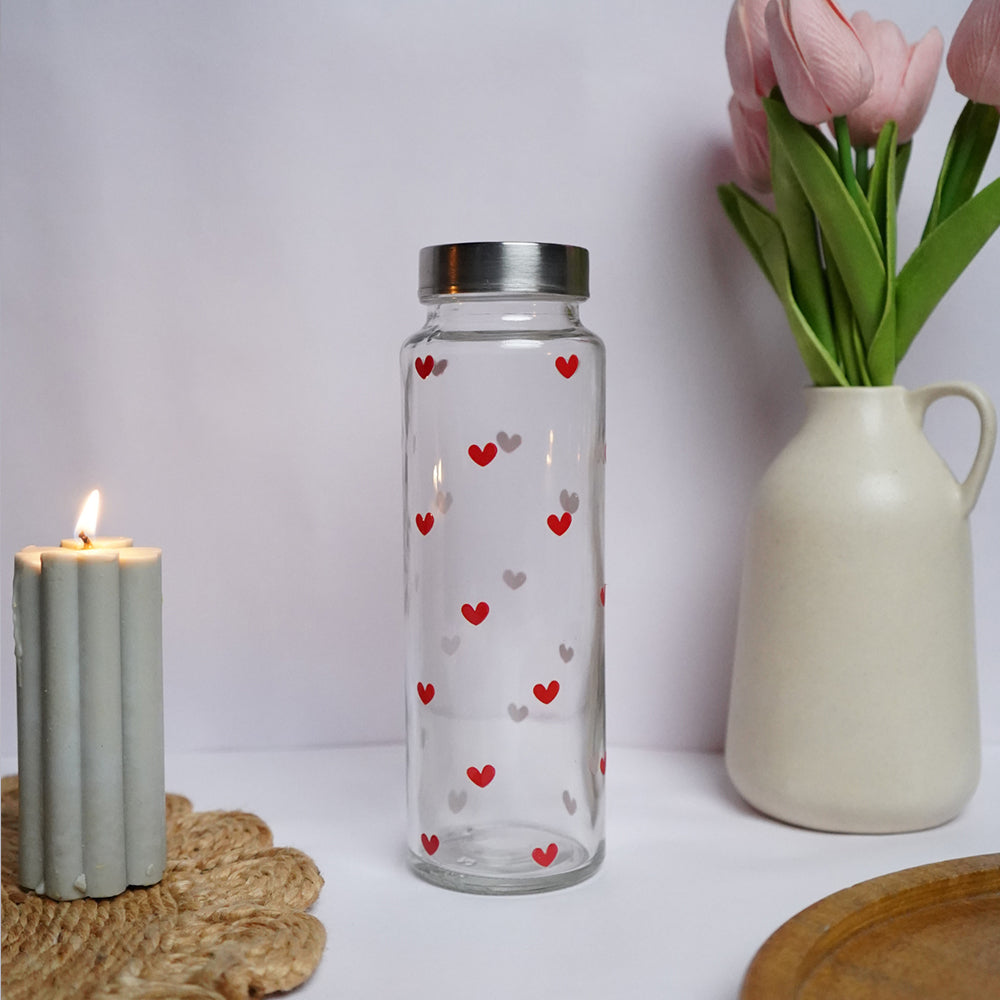 Clear glass bottle with heart patterns next to a candle and vase on a white surface