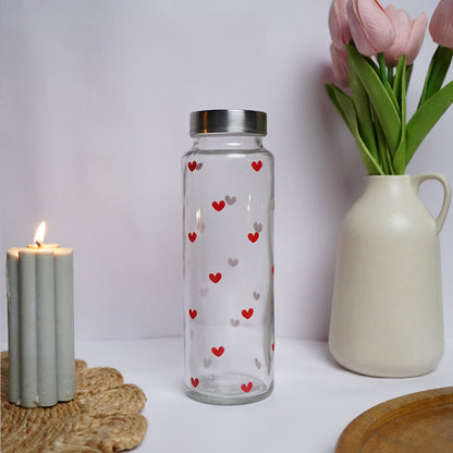Clear glass bottle with heart patterns next to a candle and vase on a white surface