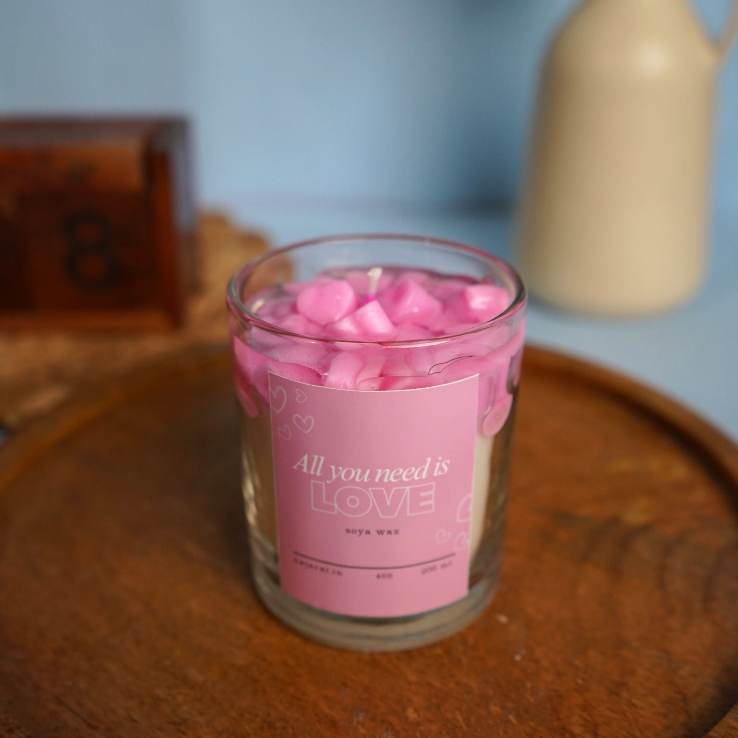 Candle jar with pink hearts on a wooden surface.