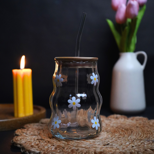 Glass candle holder with floral design on a dark background with a candle and flowers.