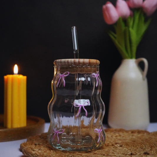 Pink Bows Glass tumbler with wooden lid on a textured surface with a candle and flowers in the background.