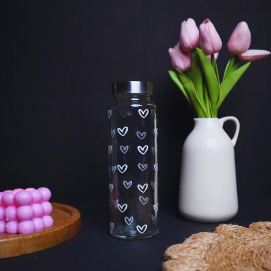 Glass bottle with heart pattern, pink tulips in a white vase, and pink candy on a dark background